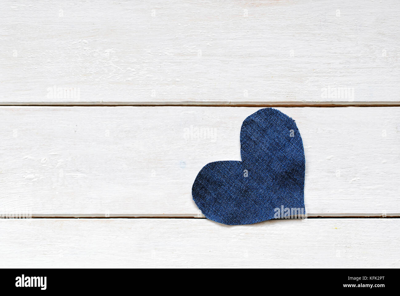 Solo cuore elegante tagliato dal blu denim bianco giace su di un tavolo di legno Foto Stock