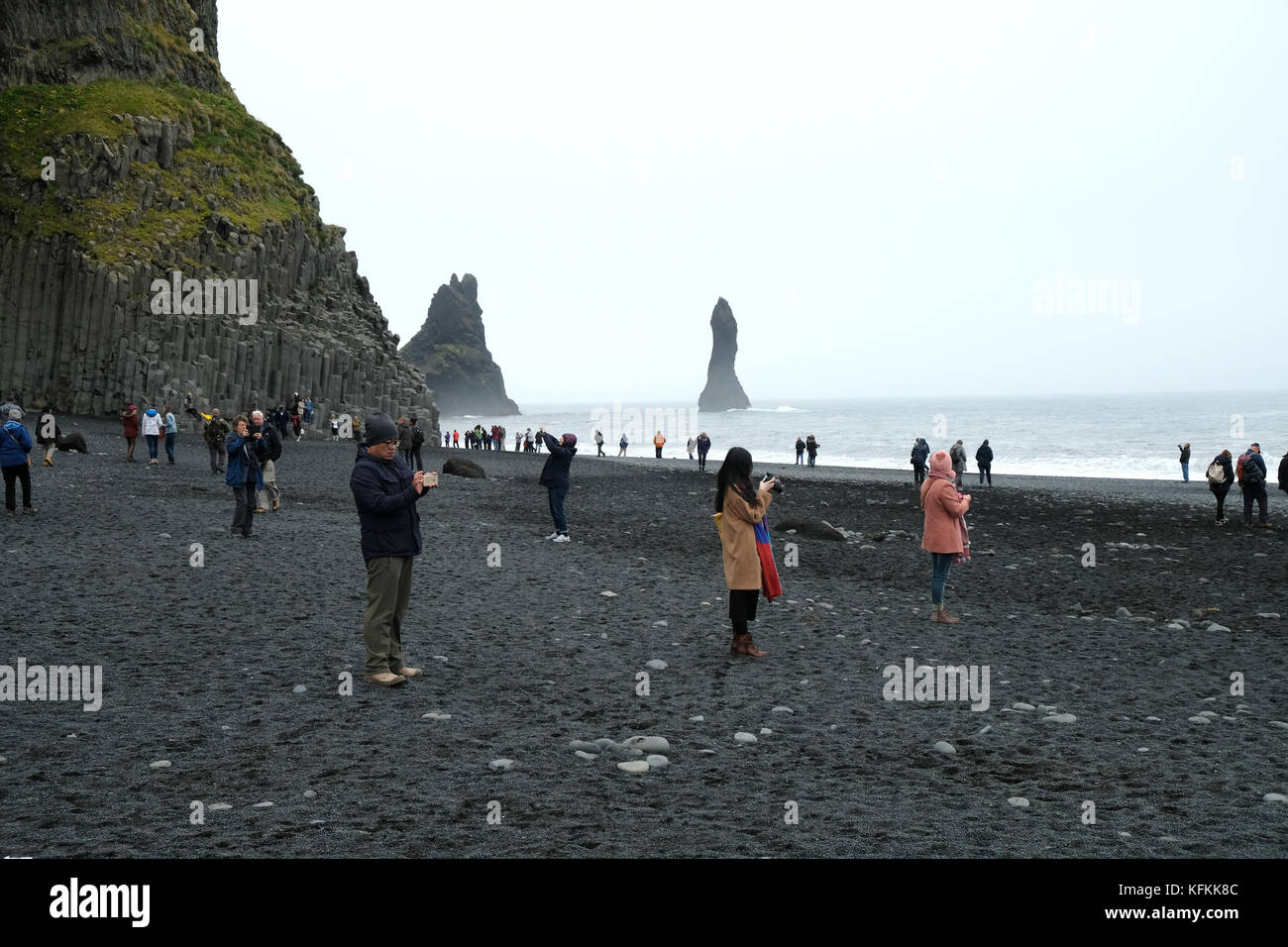Reynisfjara spiaggia di sabbia nera e maree stack con molti turisti che fotografano le tensioni di una popolare destinazione turistica sovraffollata, Vik, Islanda Foto Stock