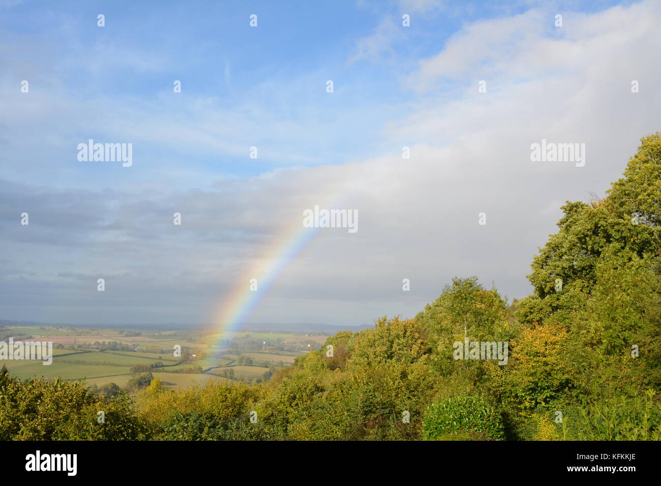 Un arcobaleno in autunno cielo blu nella campagna del South Herefordshire che si affaccia dal lato della collina con nubi alberi e altre vegetazione re clima Foto Stock