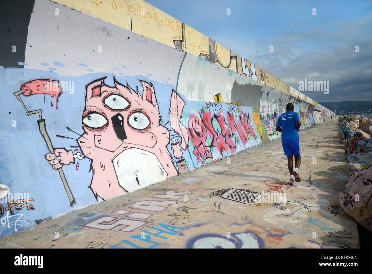 Un Jogger passa davanti a un muro di mare coperto di graffiti o a un muro di mare a la Ciotat, Bouches-du-Rhône, Provenza, Francia Foto Stock