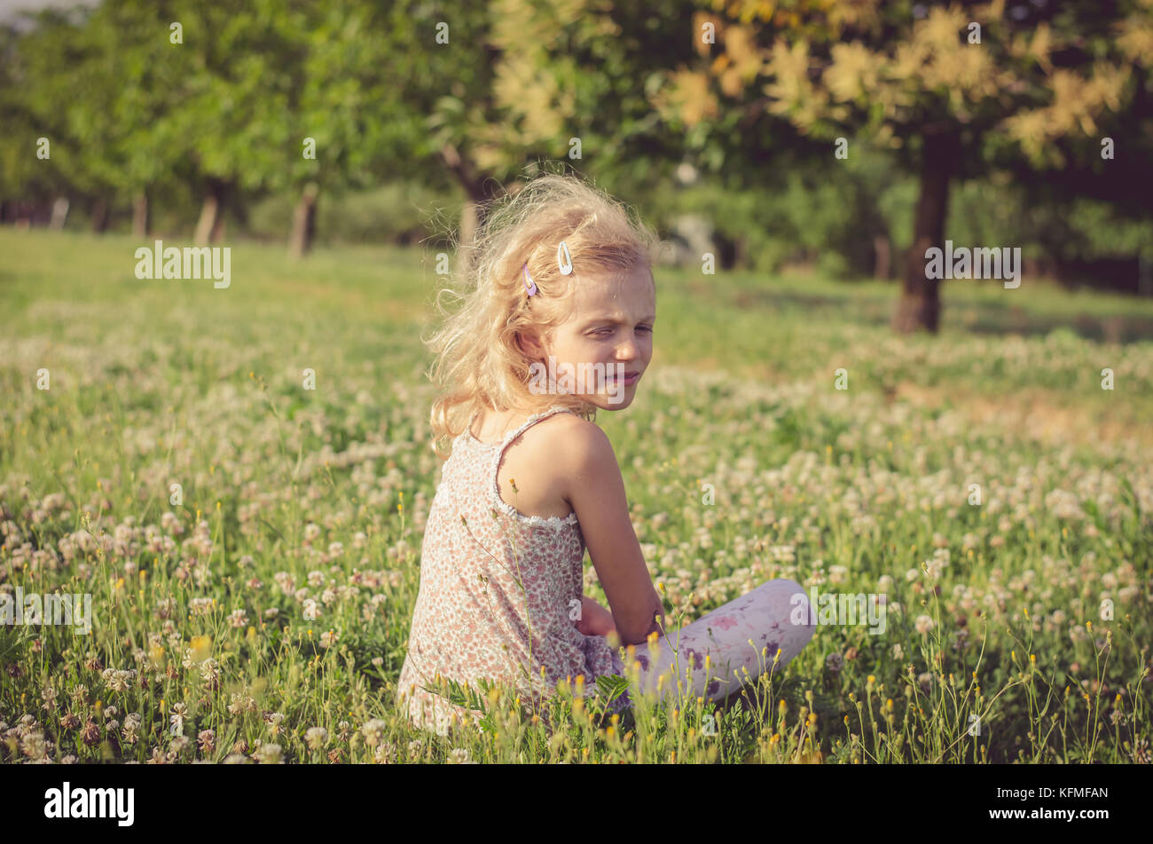 Bimba bionda seduta nella molla verde prato con la fioritura dei fiori di trifoglio Foto Stock