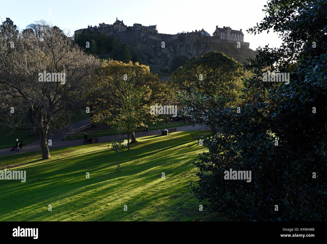 La luce solare bassa getta ombre attraverso gli alberi nei giardini di Princes street, con il Castello di Edimburgo stagliano in background. Foto Stock