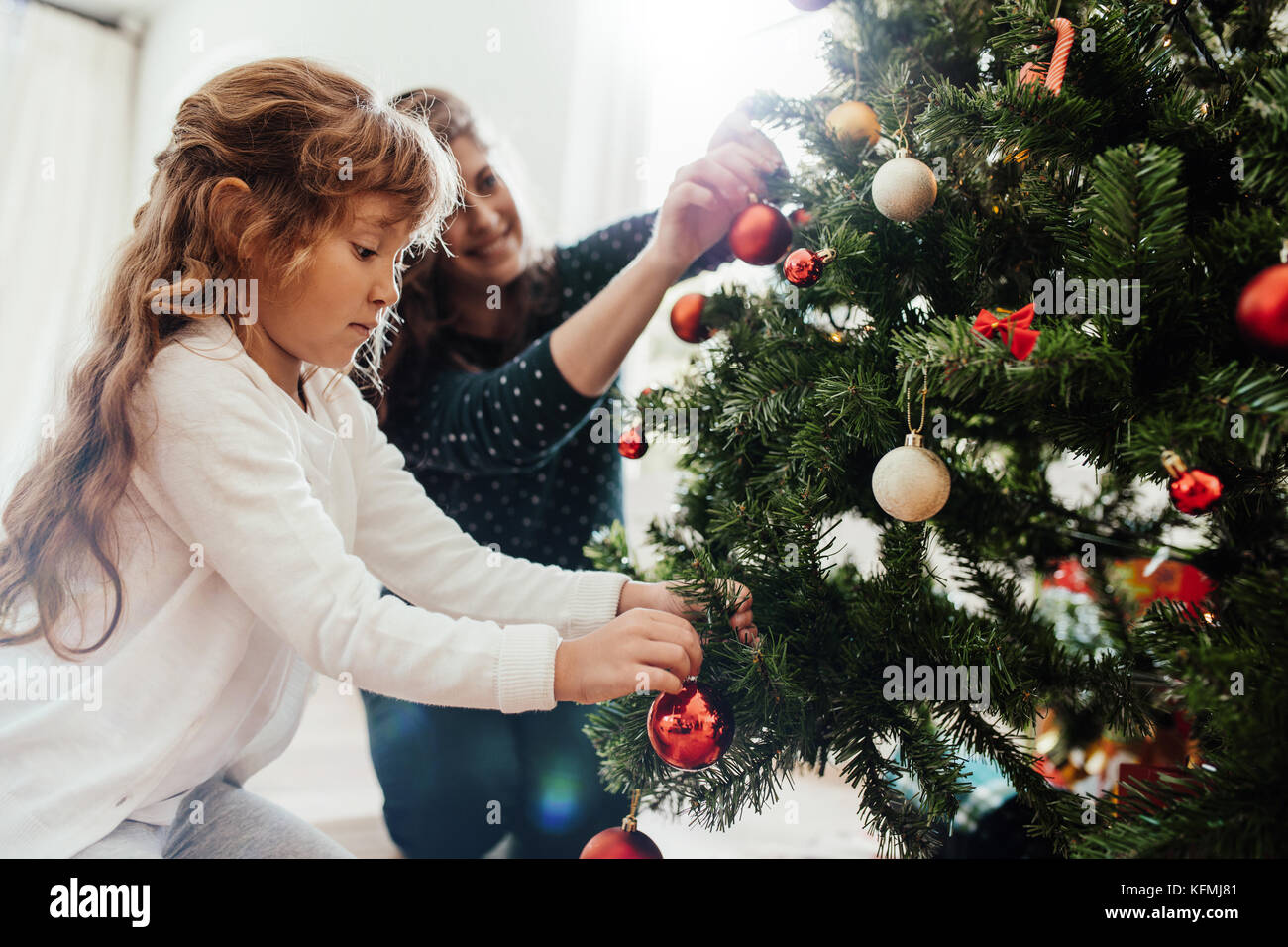 Madre e figlia piccola decorazione albero di Natale a casa. Bambina aiutando la madre nella decorazione di albero di Natale. Foto Stock