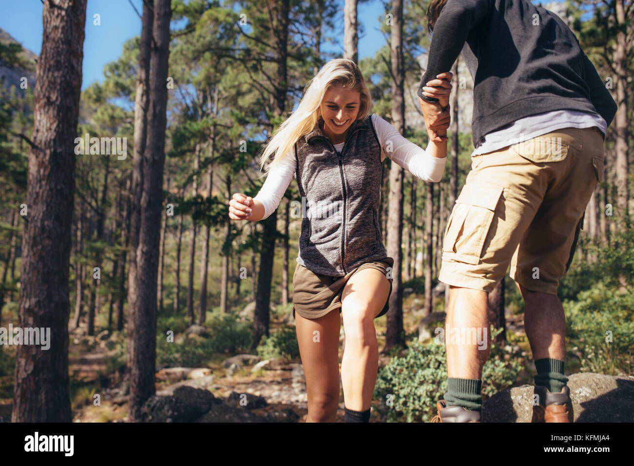 L uomo e la donna gli escursionisti trekking un sentiero roccioso nella foresta. L'uomo aiutando la sua femmina escursionismo partner salire rock mentre il trekking. Foto Stock