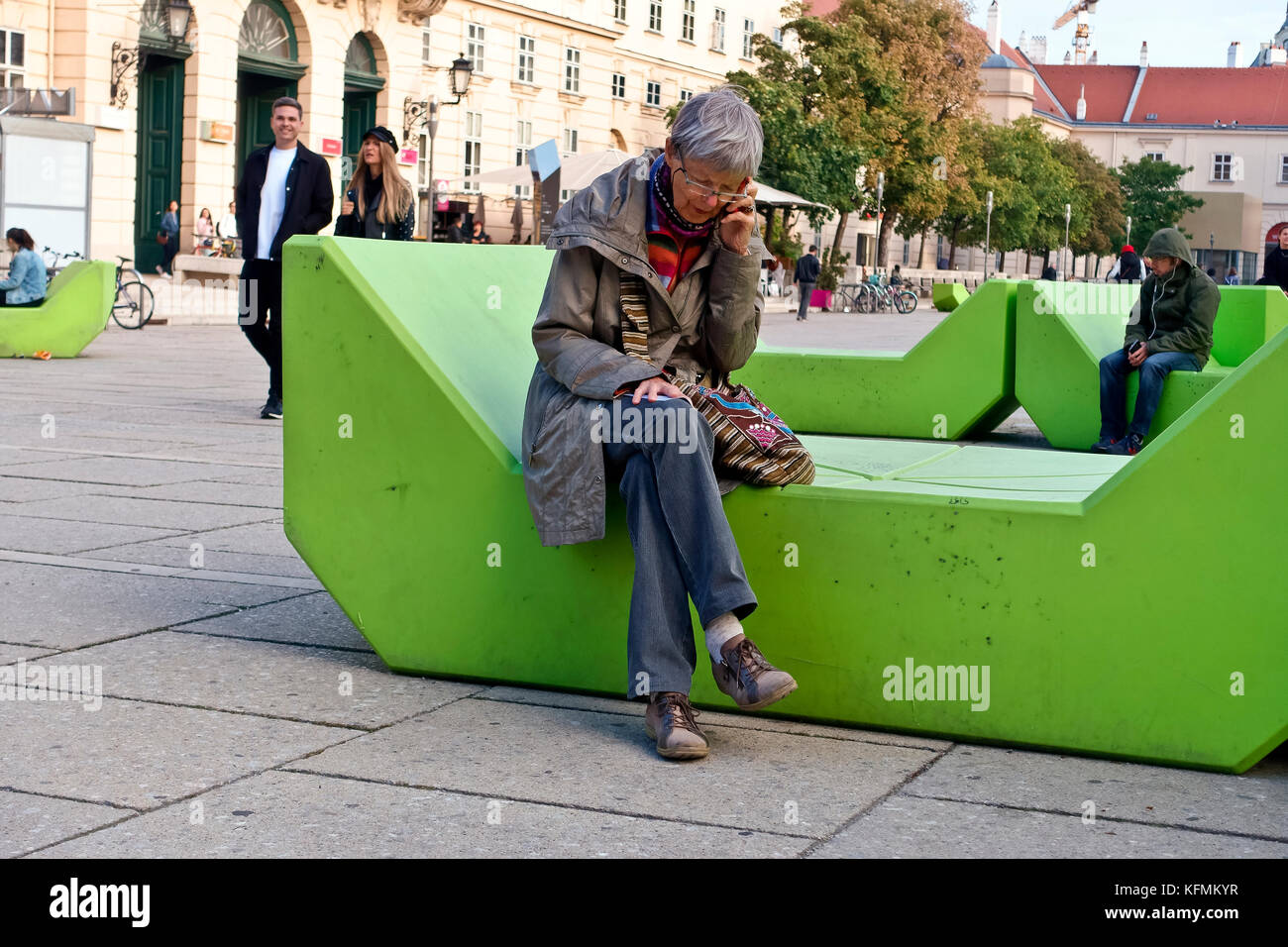 Anziana donna caucasica seduta su una moderna panchina verde a Museumsplatz, parlando sul telefono cellulare. Anziano anziano pensionato. Vienna, Austria, Europa UE Foto Stock