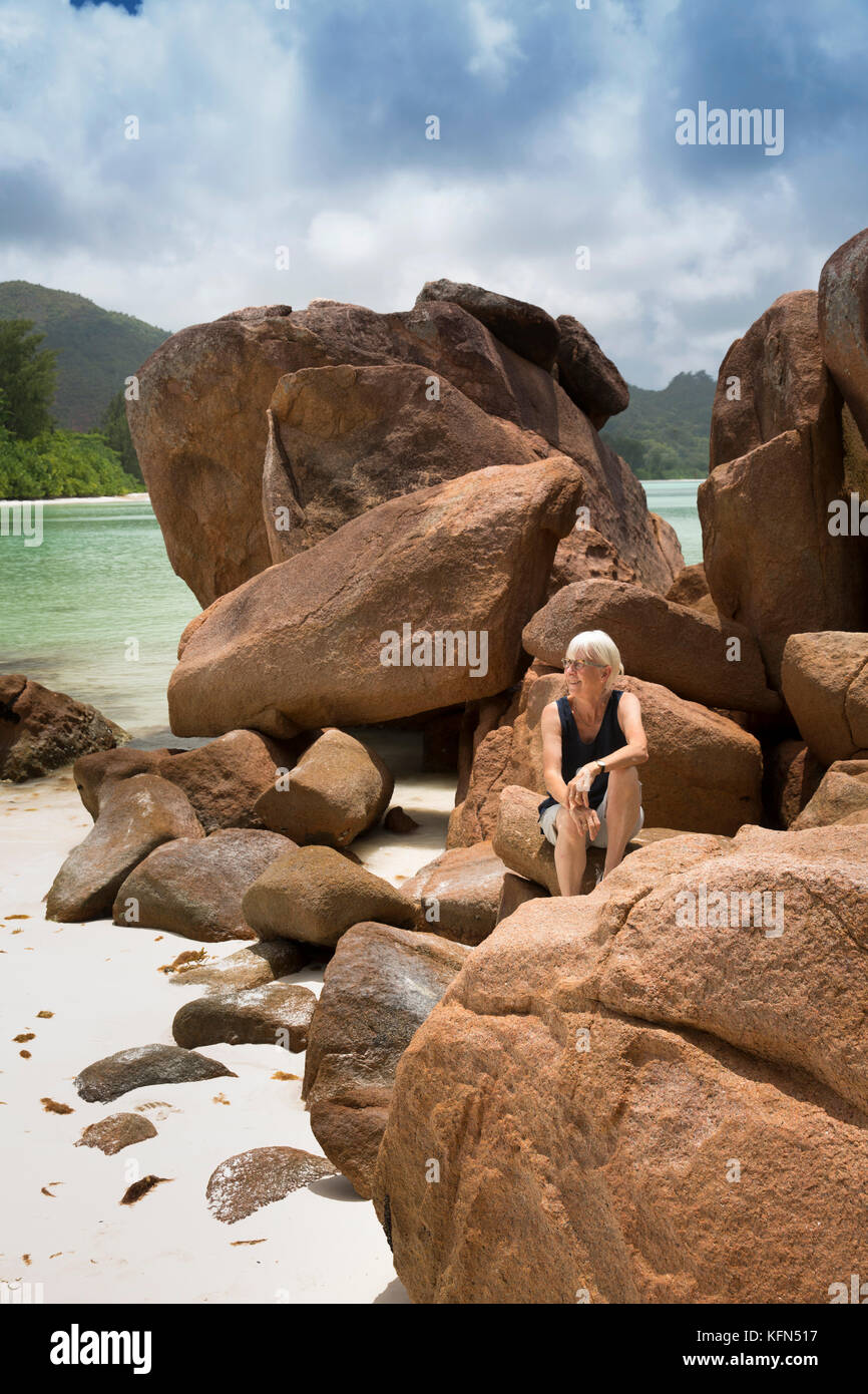 Delle Seychelles, Praslin, Anse Volbert, Cote d'Or beach donna sat sulle rocce atat Anse Tipo di governo Foto Stock