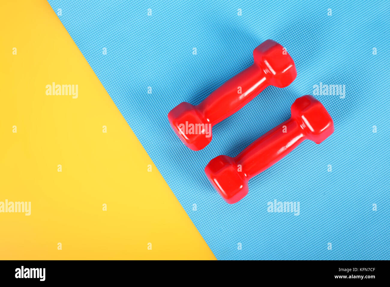 Due manubri rosso su sfondo giallo e una su un blu tappeto ginnico. Foto Stock