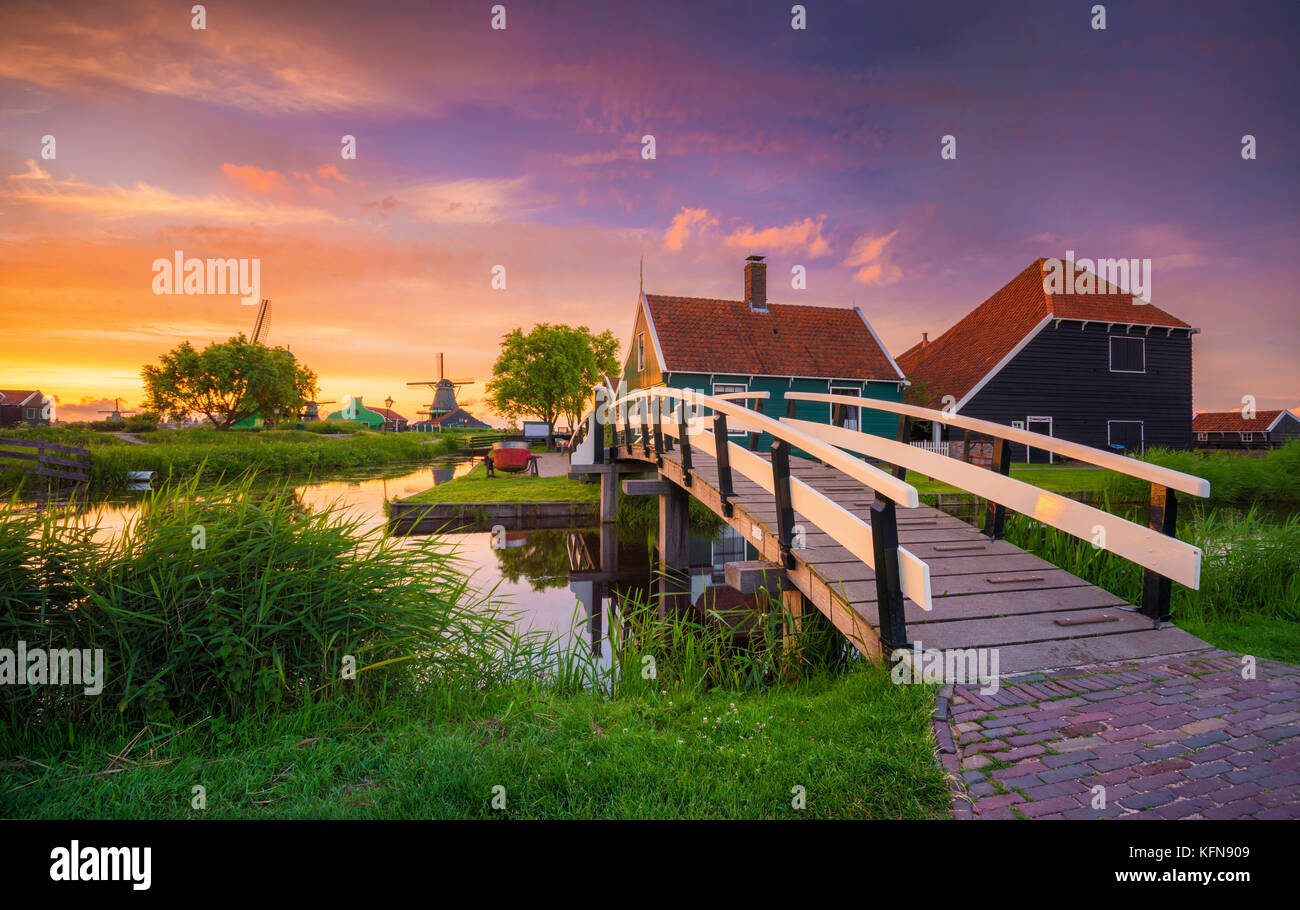 Villaggio tradizionale al tramonto, con mulini a vento olandese, il ponte e il fiume a Zaanse Schans, Holland, Paesi Bassi. Foto Stock