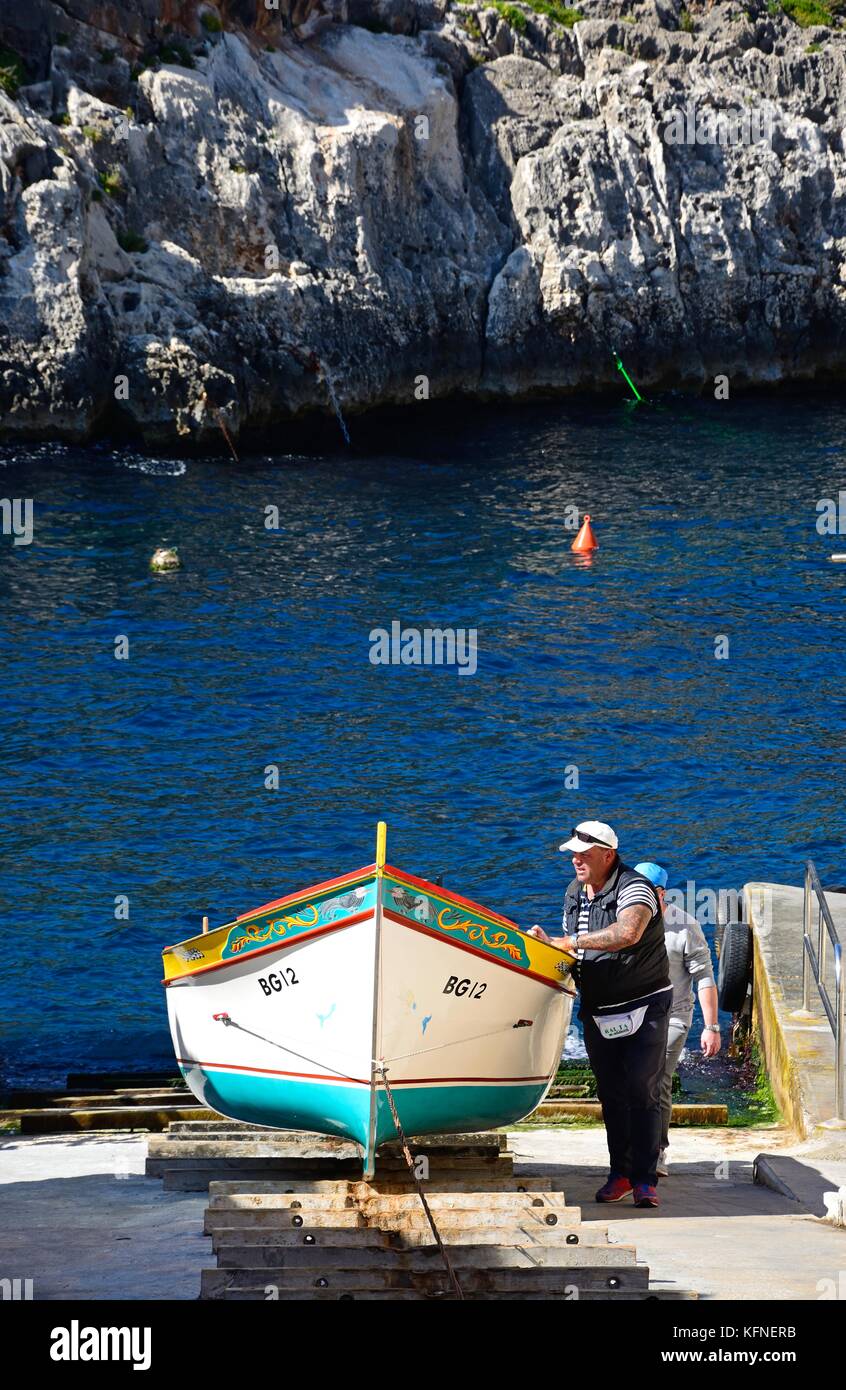 Gli uomini tirando un tradizionale dghajsa taxi acqueo fino a rampa per ormeggio presso il punto di partenza, Blue Grotto, Malta, l'Europa. Foto Stock