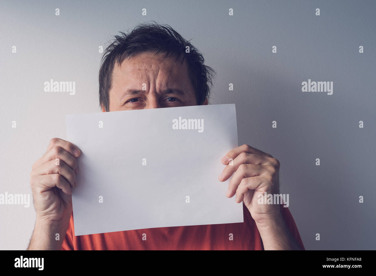 L'uomo nascosto dietro vuoto carta bianca come copia di spazio per un messaggio di testo Foto Stock
