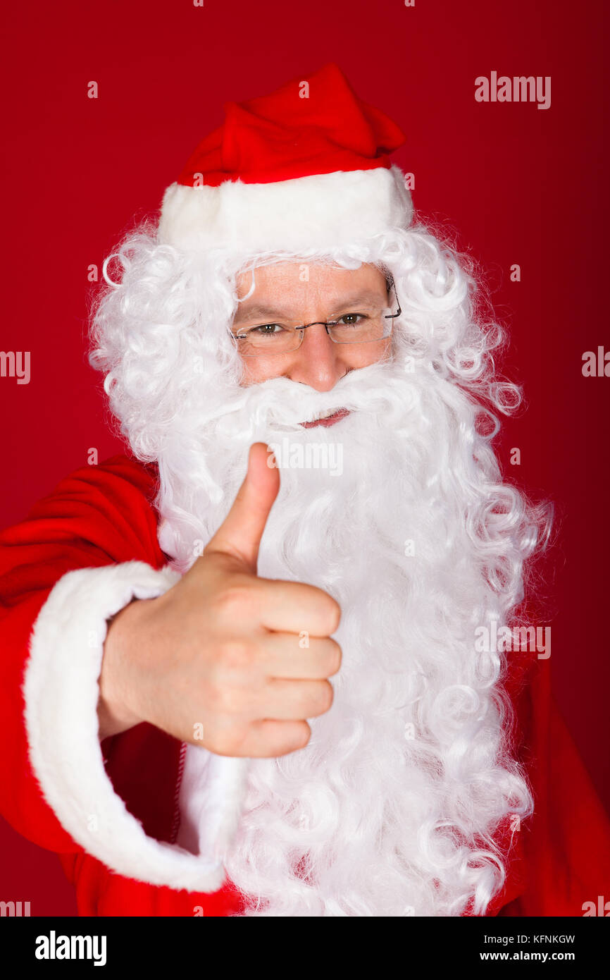 Ritratto di felice santa gesticolando pollice su sfondo rosso Foto Stock