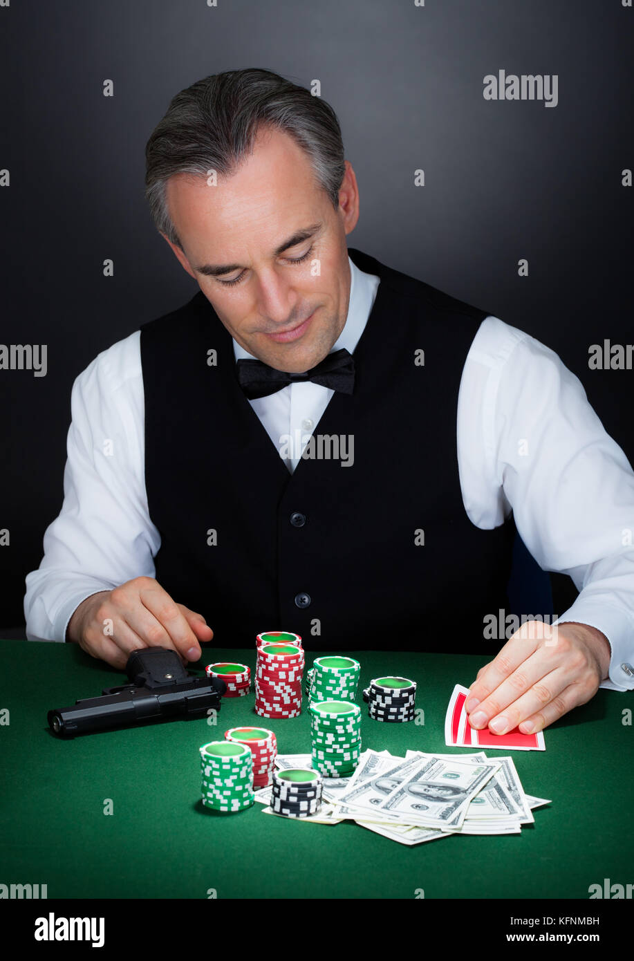 Ritratto di un croupier che guarda carte da gioco con pistola e pila di chip Foto Stock
