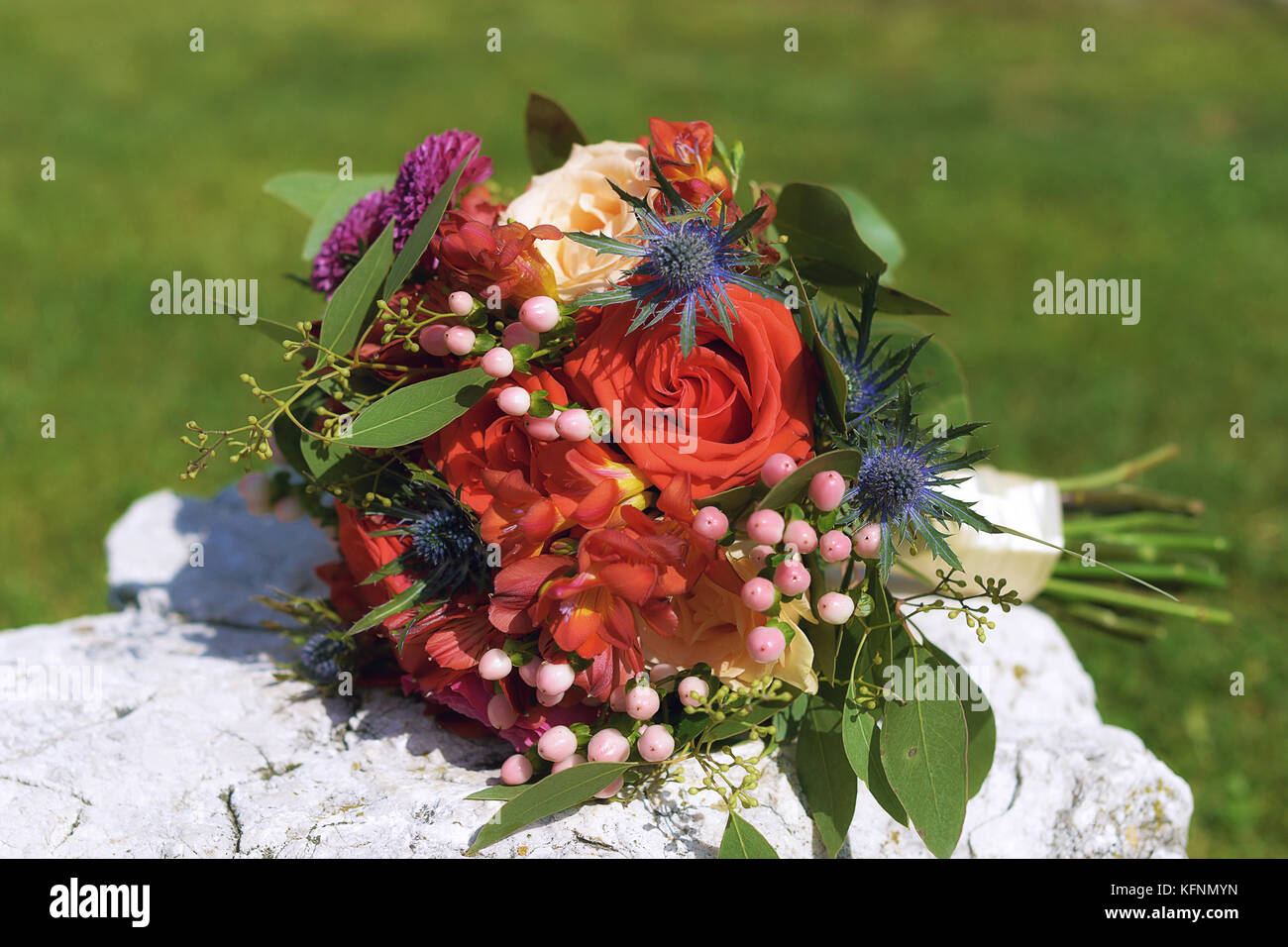 Riflessi aranciati Bouquet nozze con freesias, rose e bacche posizionata su di una roccia bianca sotto la luce diretta del sole Foto Stock