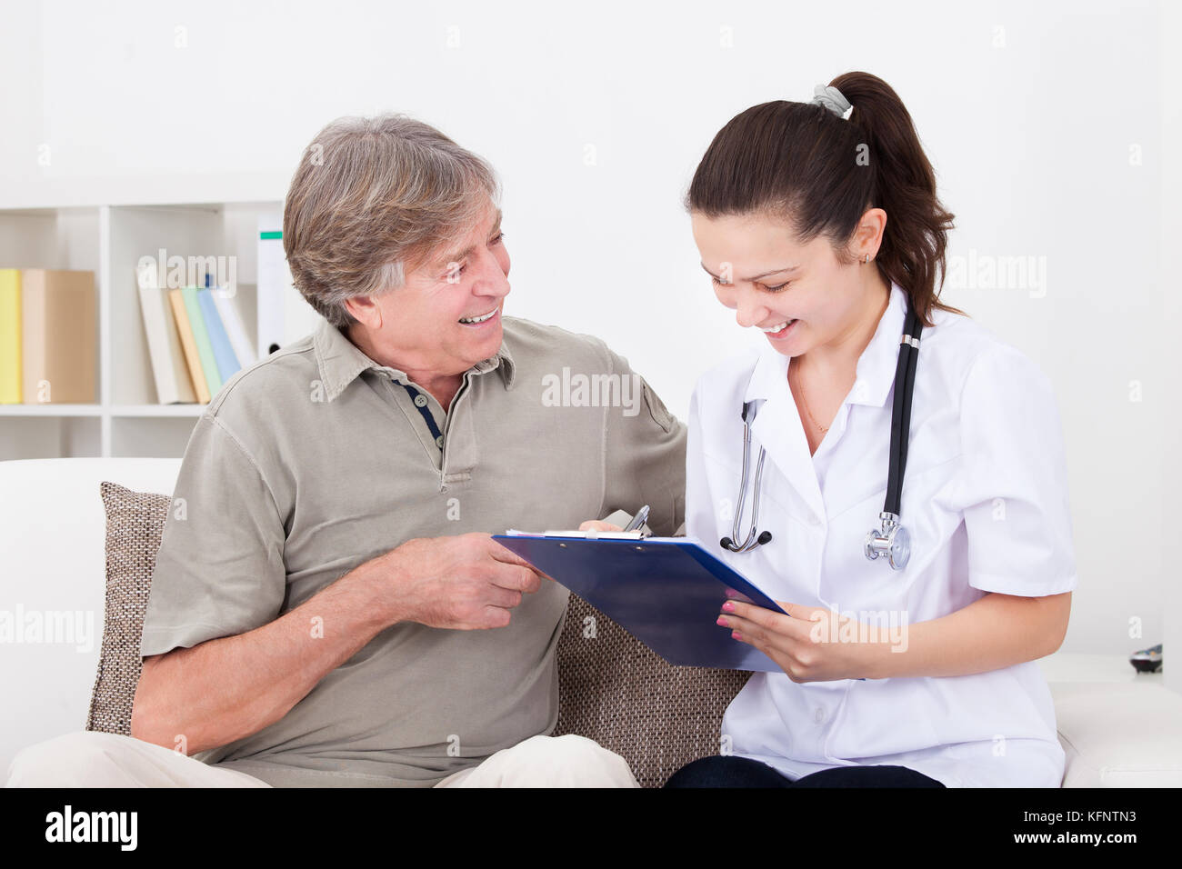 Felice medico donna seduta con paziente sul lettino iscritto negli appunti Foto Stock