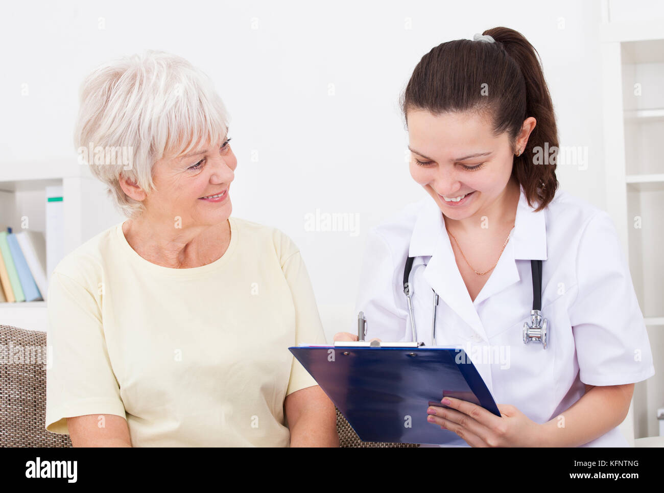 Giovani donne medico iscritto negli appunti seduta con paziente senior Foto Stock