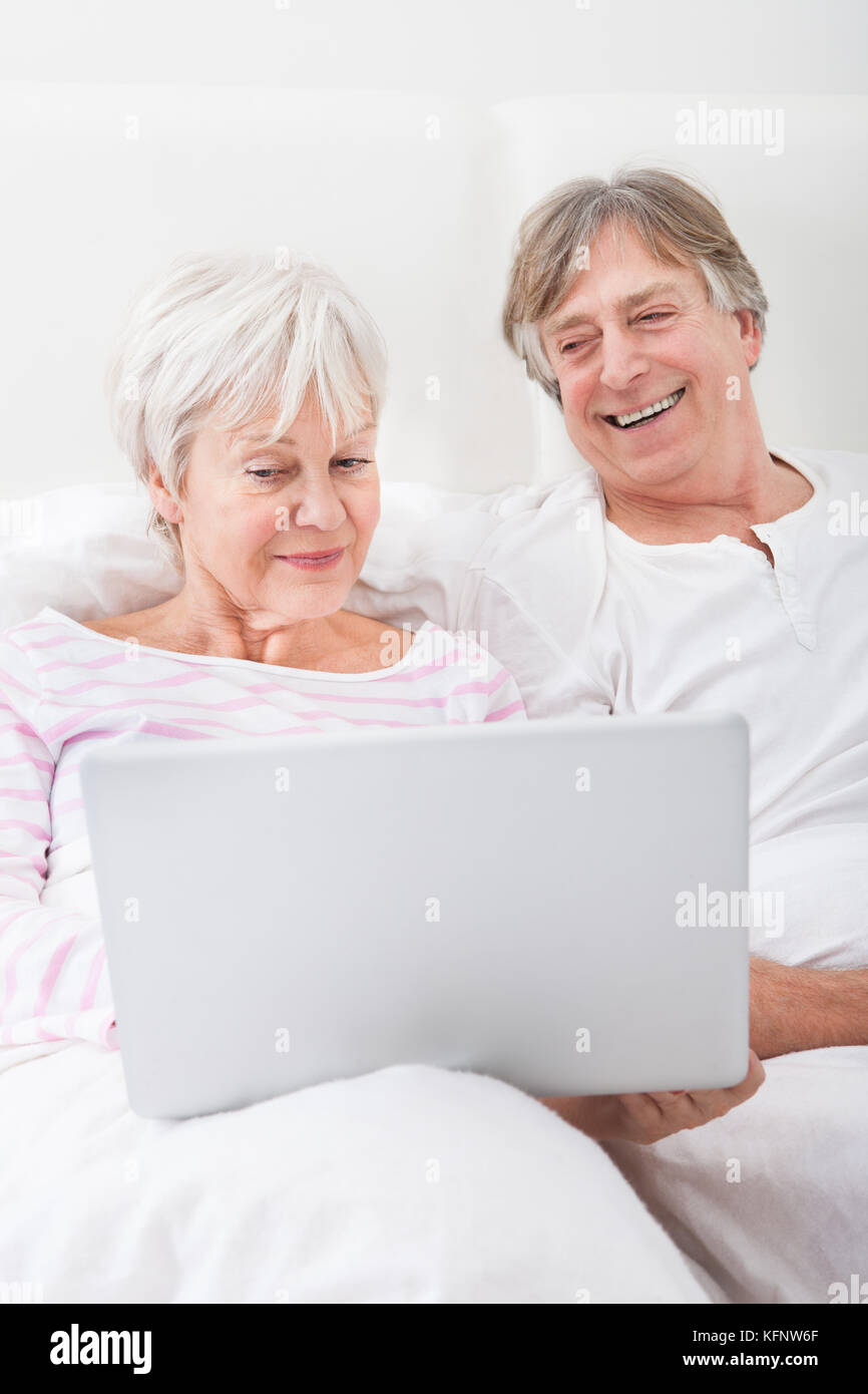 Ritratto di felice coppia Senior giacente sul letto guardando al laptop Foto Stock