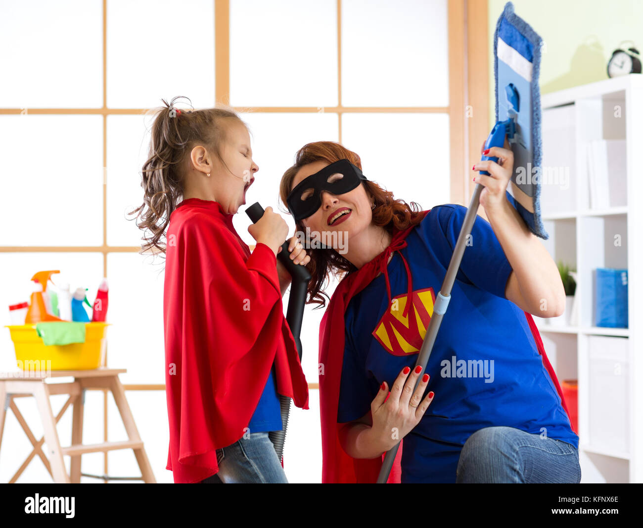 Il concetto di pulizia. super eroe donna e la figlia a suonare la chitarra e cantare su apparecchiature di pulizia. famiglia pronta per la pulizia. Foto Stock