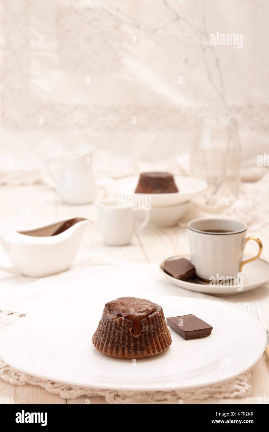 Il cioccolato francese dessert torta mi-cuit sulla piastra bianca sulla tovaglia bianca, una tazza di caffè, sauceboat con salsa di cioccolato, latte jar, cioccolato piec Foto Stock