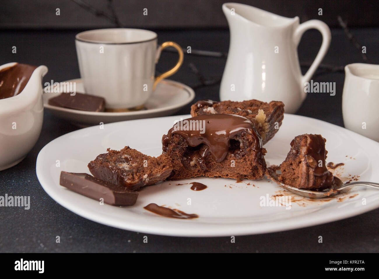 Il cioccolato francese dessert torta mi-cuit sulla piastra bianca sulla tovaglia bianca, una tazza di caffè, sauceboat con salsa di cioccolato, latte jar, cioccolato piec Foto Stock