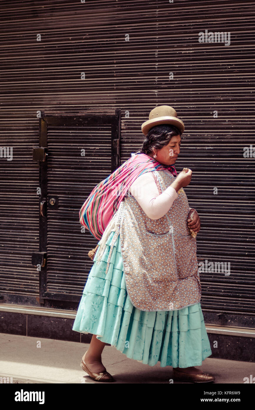 Una donna è visto camminare per le strade di La Paz, indossa gli abiti tradizionali e la peculiare hat. La Paz, Bolivia Foto Stock