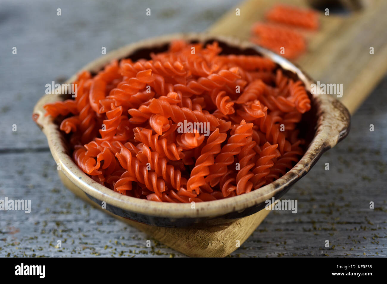 Primo piano di un vaso di terracotta pieno di crudo di lenticchie rosse fusilli sul grigio di una tavola in legno rustico Foto Stock