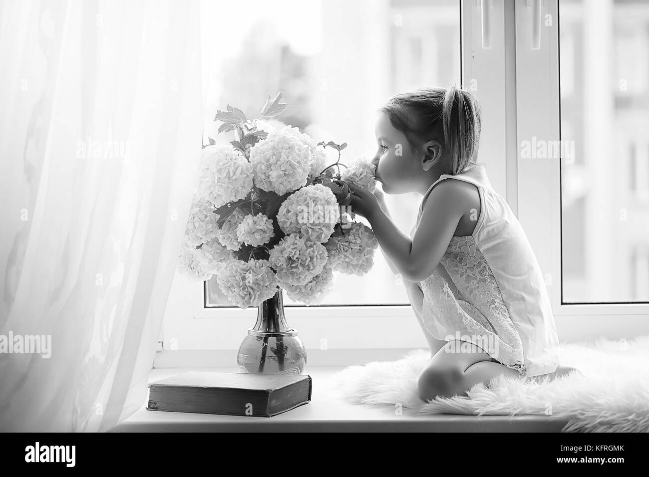 La bambina è seduta sul davanzale. un mazzo di fiori Foto Stock