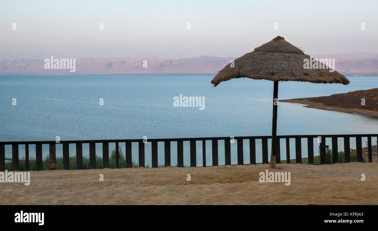 Presto la luce del mattino al Holiday Inn Dead Sea resort, nessun popolo sulla spiaggia e la vista sul Mar Morto, con paglia ombrellone, Giordania, Medio Oriente Foto Stock