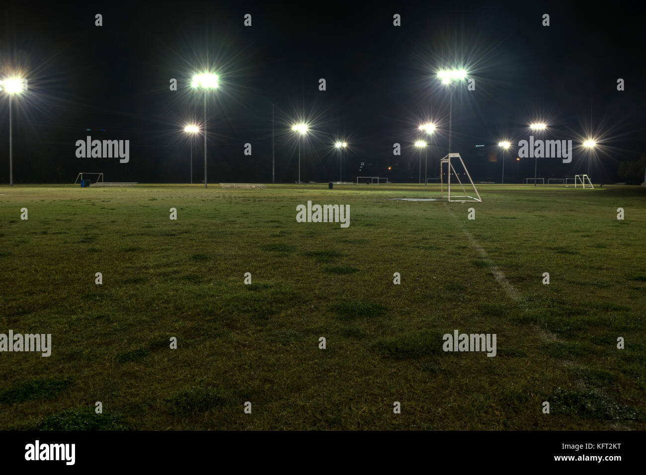 Obiettivo e vuoti i campi di calcio durante la notte con le luci illuminano l'erba verde e riflettendo l'acqua scende da un recente pioggia. Foto Stock