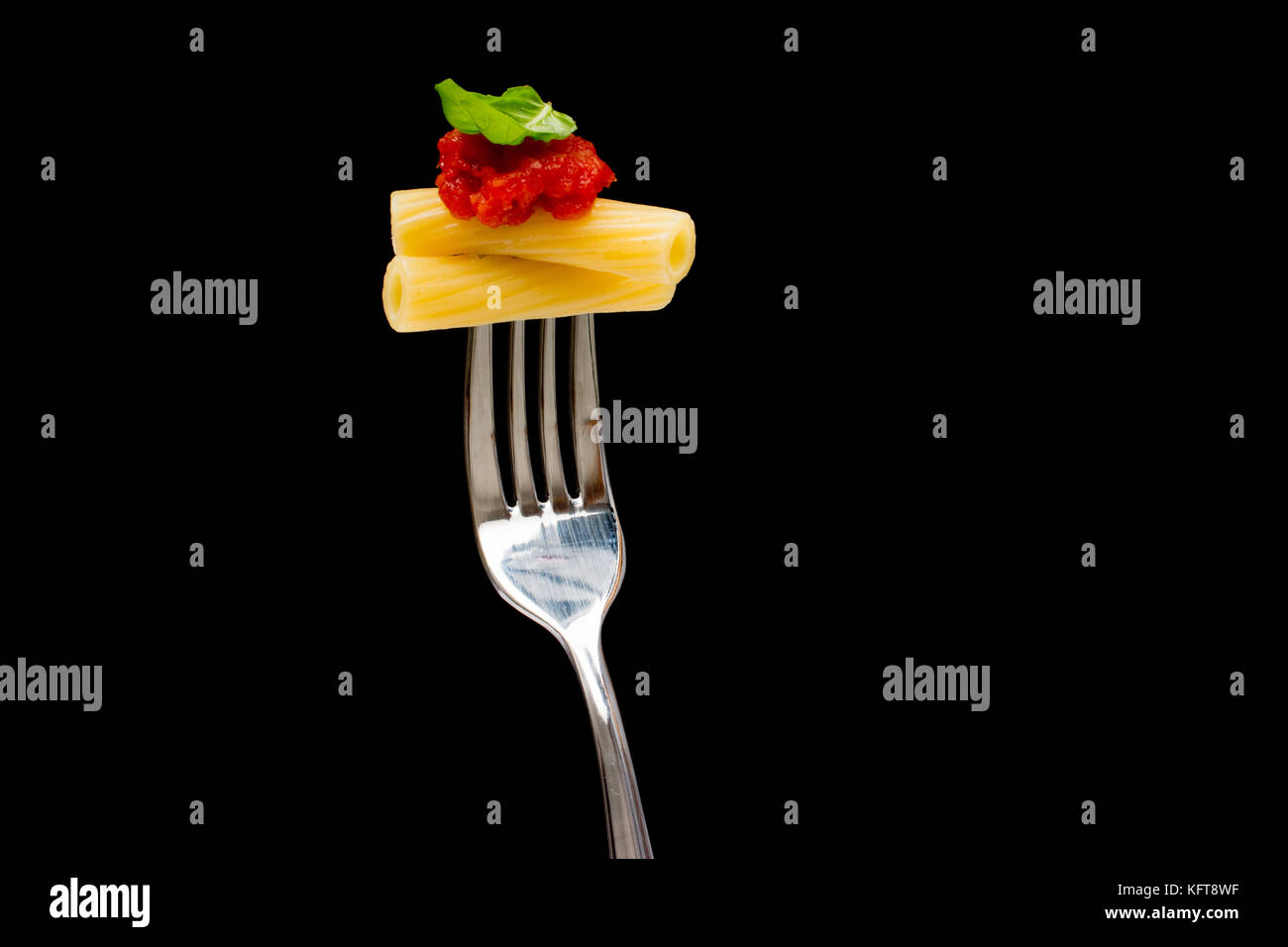 La pasta in sfondo nero. rigatoni, pomodoro e basilico sulla forcella. cucina italiana concept Foto Stock