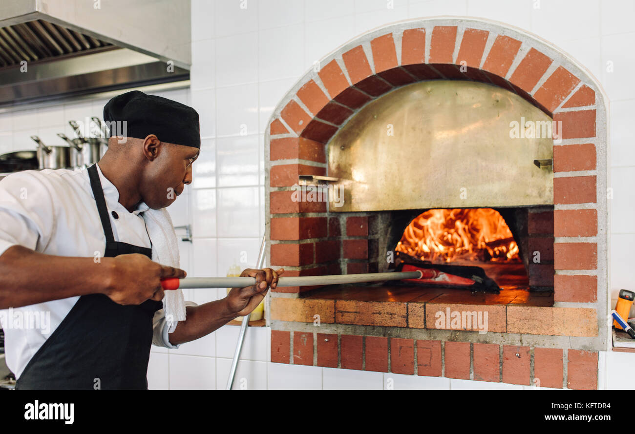 Lo Chef cuocere la pizza in forno a legna in cucina commerciale. Cuocere la pizza di cottura in un forno tradizionale in pietra al ristorante. Foto Stock