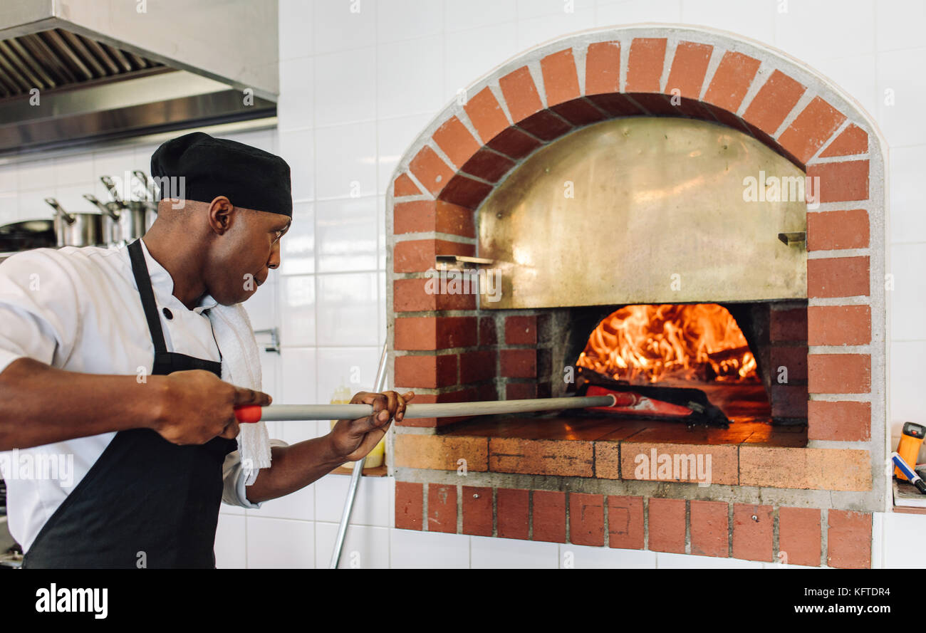 Lo Chef cuocere la pizza in forno a legna in cucina commerciale. Cuocere la  pizza di cottura in un forno tradizionale in pietra al ristorante Foto  stock - Alamy