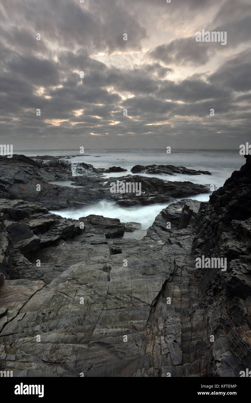 La bella atmosfera litorale della Cornovaglia a Constantine Bay vicino a Padstow in Cornovaglia del nord con il mare di schiantarsi sulla roccia come nebbia al tramonto Foto Stock