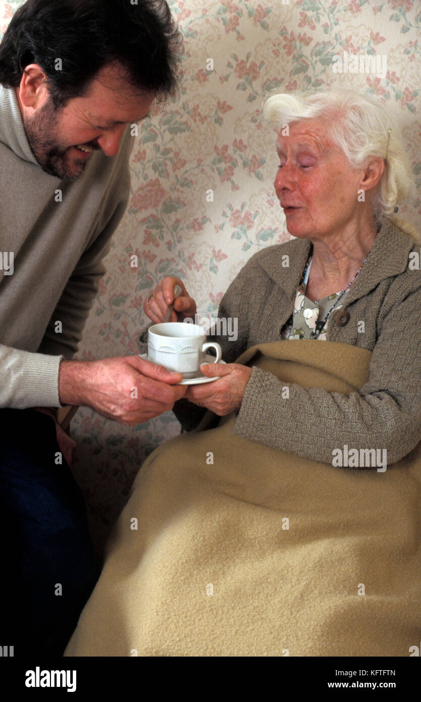 L'uomo/accompagnatore/figlio consegna tazza di tè a geriatrica lady in casa di cura Foto Stock