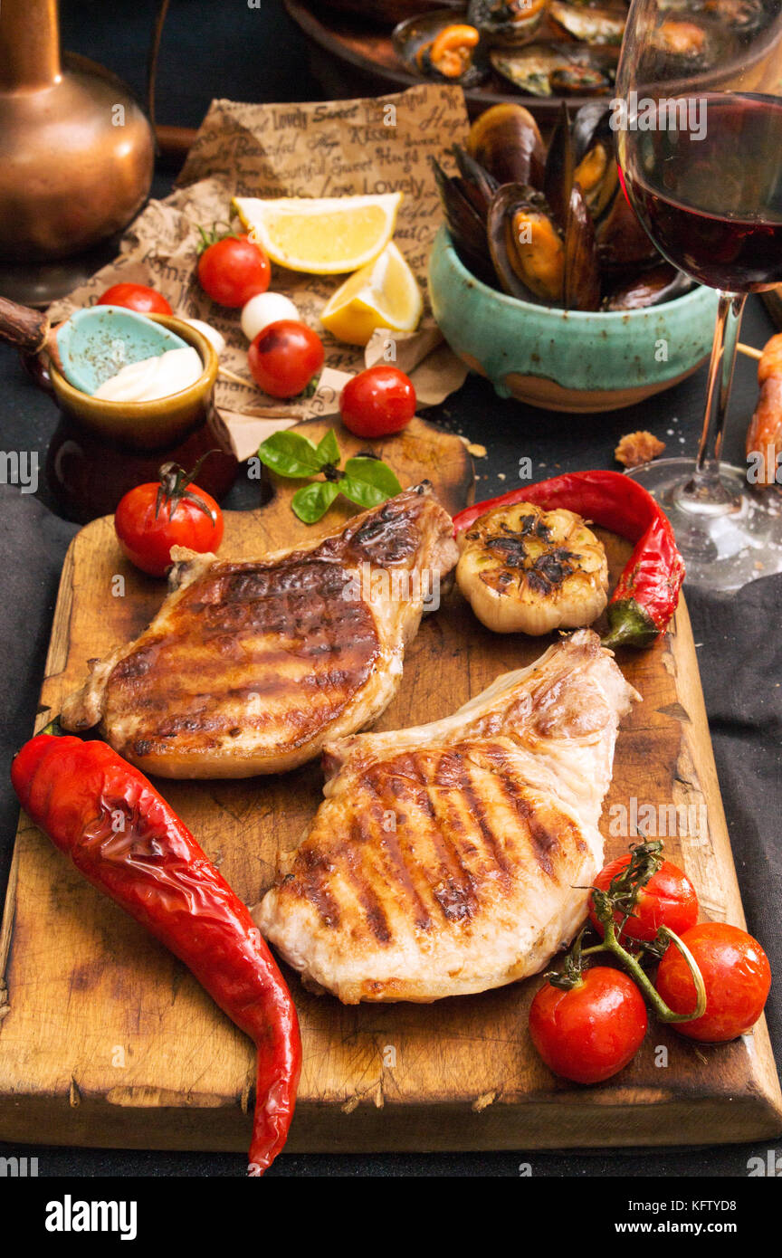 Overhead del tavolo per la cena. Un assortimento di deliziosi barbecue grigliate di carne e pesce con verdure. La carne di maiale bistecche ai ferri, salmone alla griglia trota, cozze, SHR Foto Stock