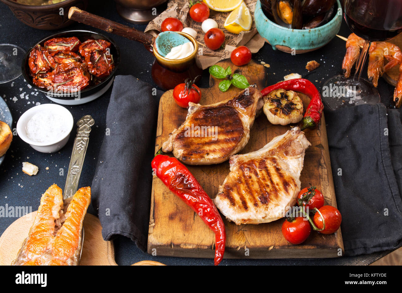 Overhead del tavolo per la cena. Un assortimento di deliziosi barbecue grigliate di carne e pesce con verdure. La carne di maiale bistecche ai ferri, salmone alla griglia trota, cozze, SHR Foto Stock