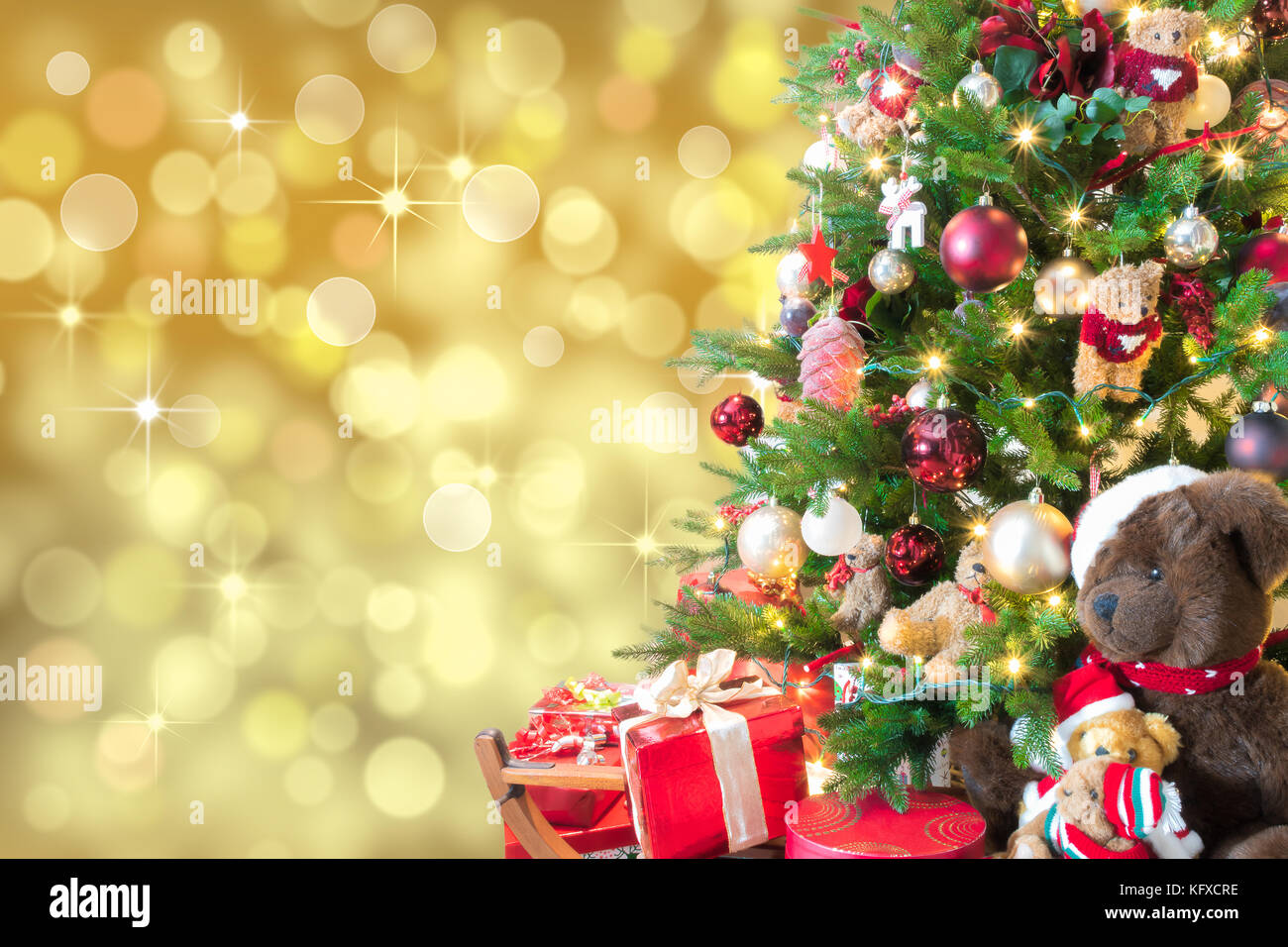 Oro sullo sfondo di Natale con luci sfocati, albero di Natale decorato, confezione regalo rossa e orsacchiotti. Foto Stock