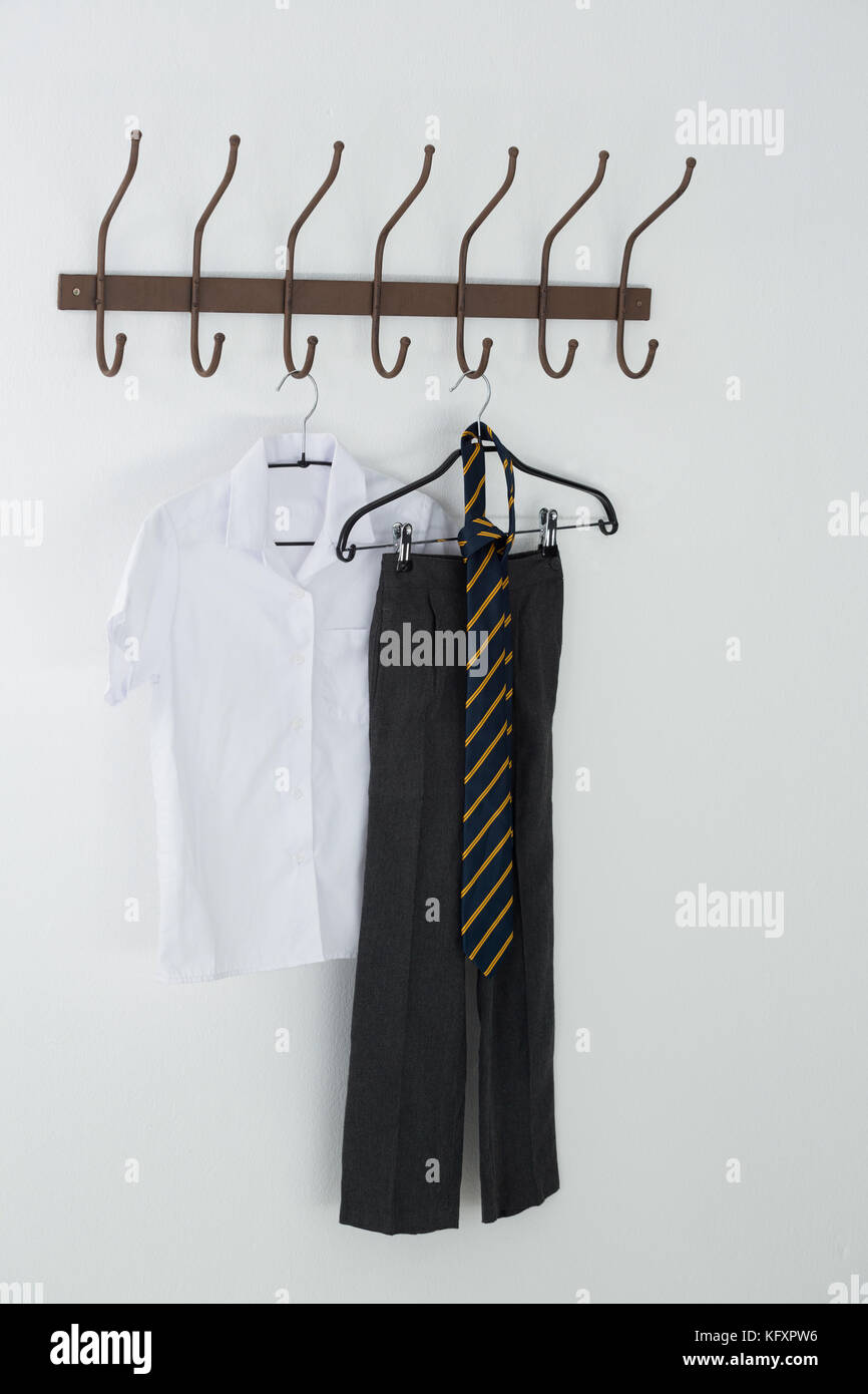 Maglietta formale, cravatta e pantaloni appesi a gancio contro il muro bianco Foto Stock