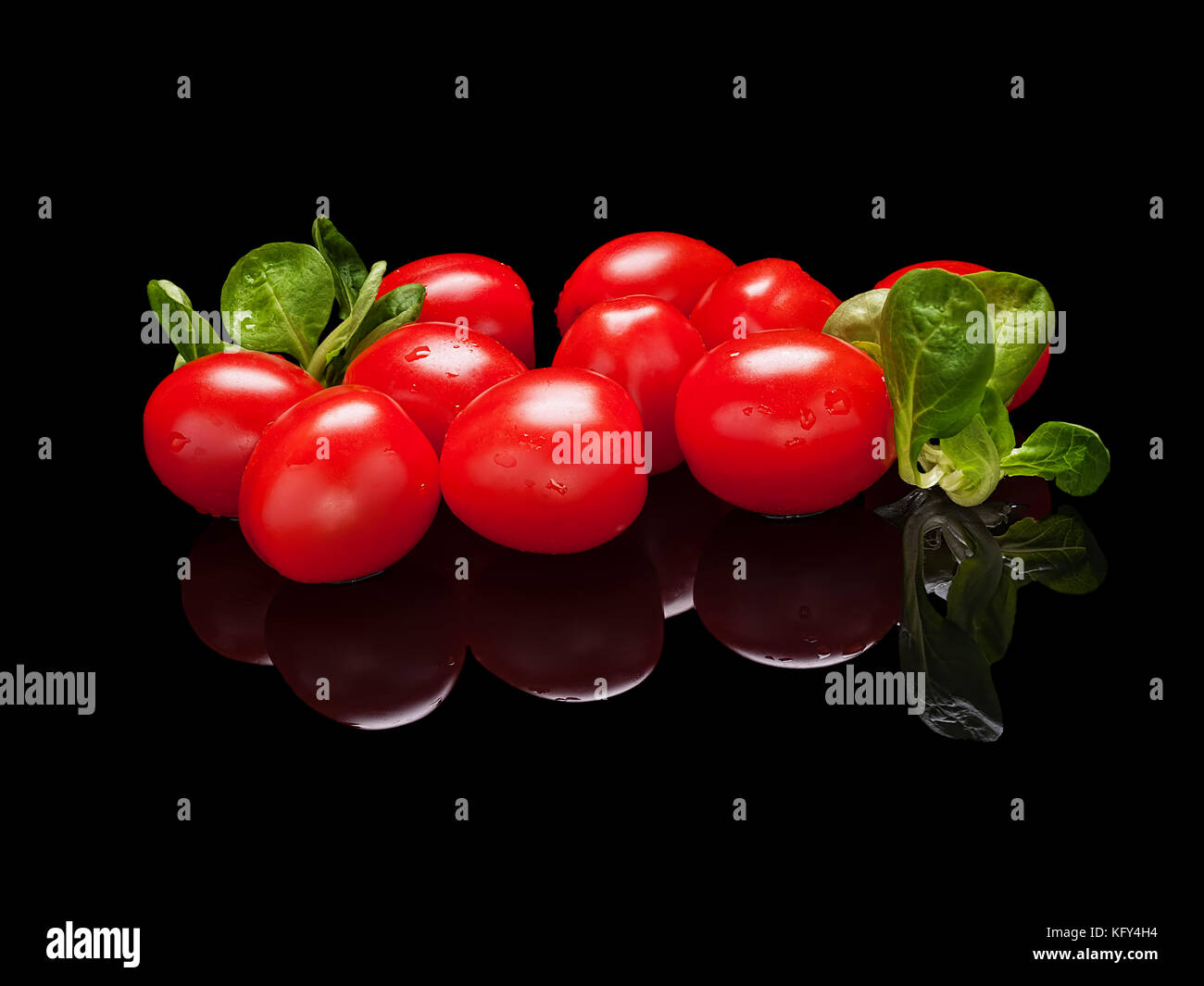 Mazzetto di piccoli pomodori rossi con foglie di lattuga isolato nero su sfondo lucido con una vera riflessione. vista laterale Foto Stock