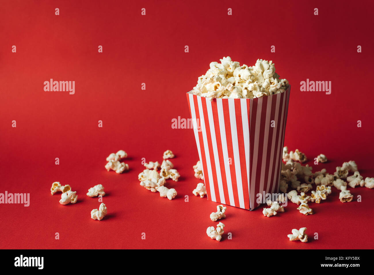 Scatola a strisce con popcorn su sfondo rosso Foto Stock
