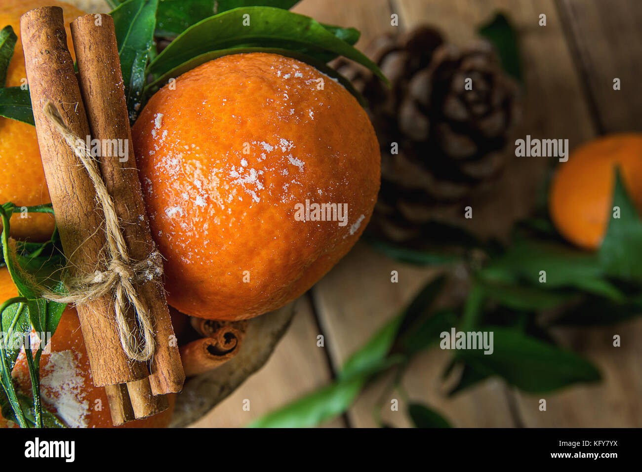 Arancione brillante tangerini sui rami verdi foglie bastoncini di cannella legata con lo spago pigna sparsi su uno sfondo di legno. Natale Capodanno Saluto Foto Stock