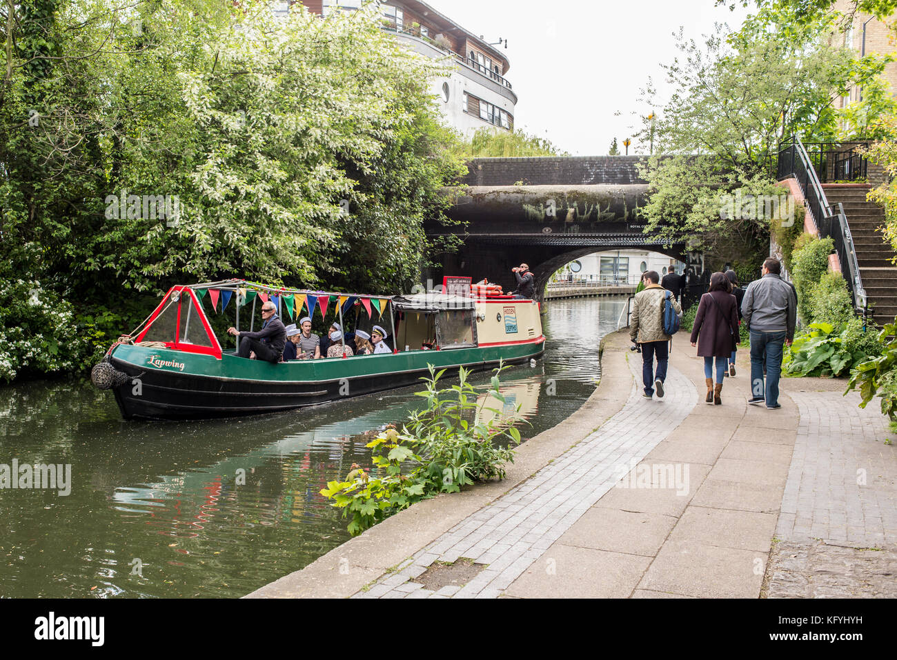 Barca o chiatta che passa sul Regents Canal con persone che camminano nel sentiero di città vicino a Camden Town, Londra, Inghilterra, Regno Unito Foto Stock