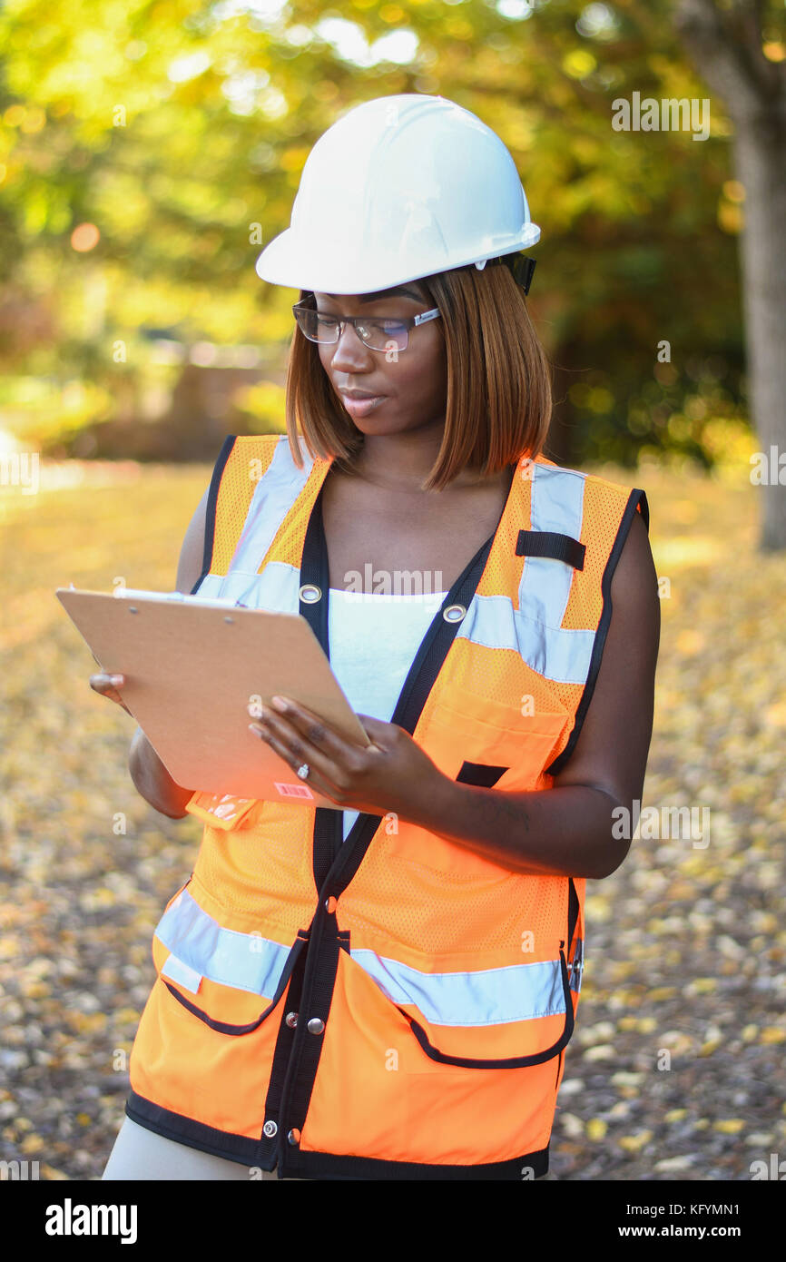 Una femmina nero lavoratore edile che indossa un cappello bianco e arancione vest lavorando al di fuori di un parco della città Foto Stock