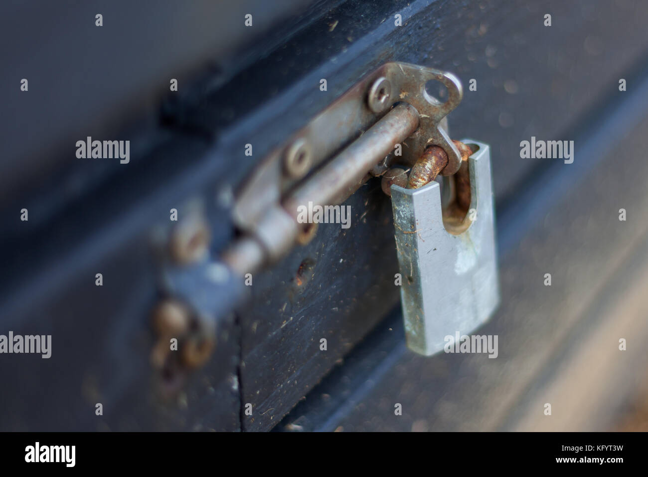 Un blocco lucchetto arrugginito su un catenaccio scorrevole fermo nella posizione di bloccaggio su una scatola di legno Foto Stock