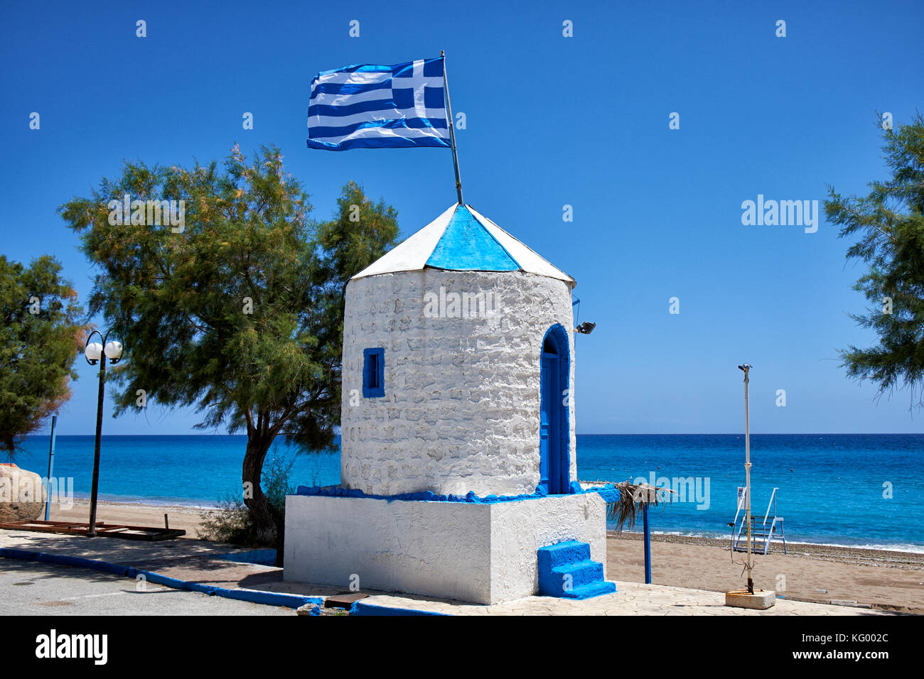 Bandiera Greca battenti sul tetto del mulino a vento ridondante dipinte in nazionale greco di colori blu e bianco alla spiaggia stagna, Archangelos, Rodi, Grecia Foto Stock