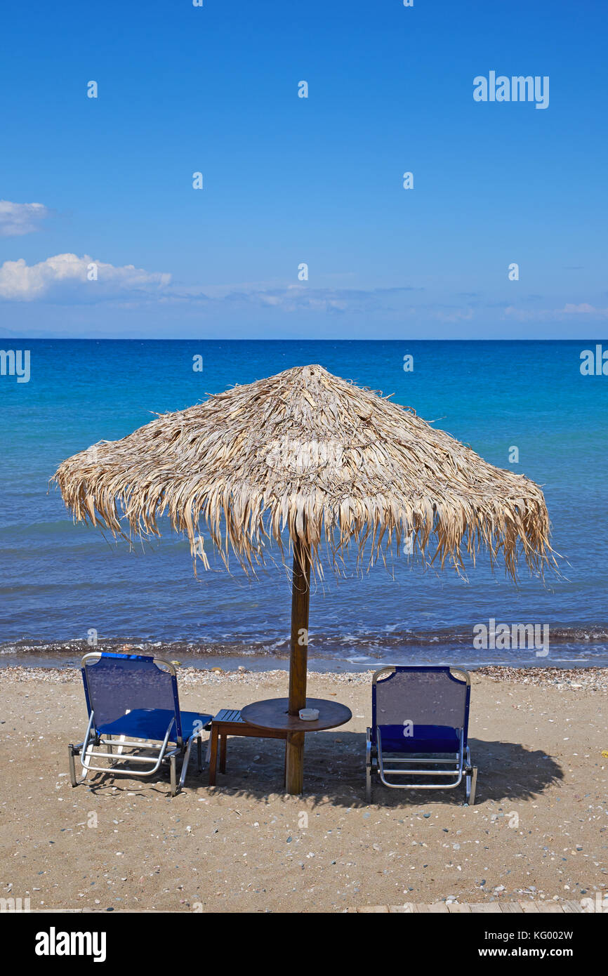 Vacante sedie a sdraio sotto un ombrellone sulla spiaggia dell'isola di Rodi, Grecia Foto Stock