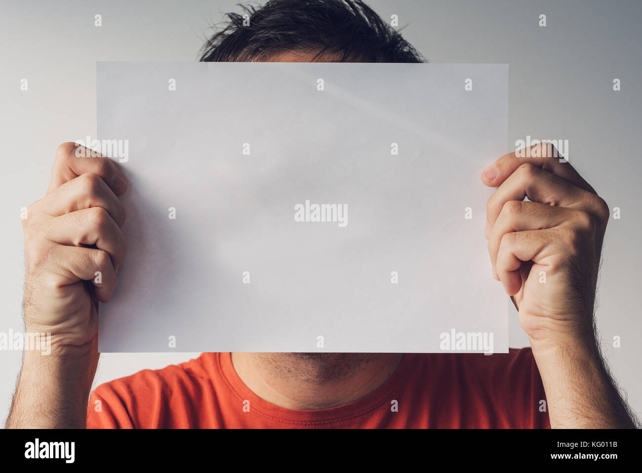 L'uomo nascosto dietro vuoto carta bianca come copia di spazio per un messaggio di testo Foto Stock