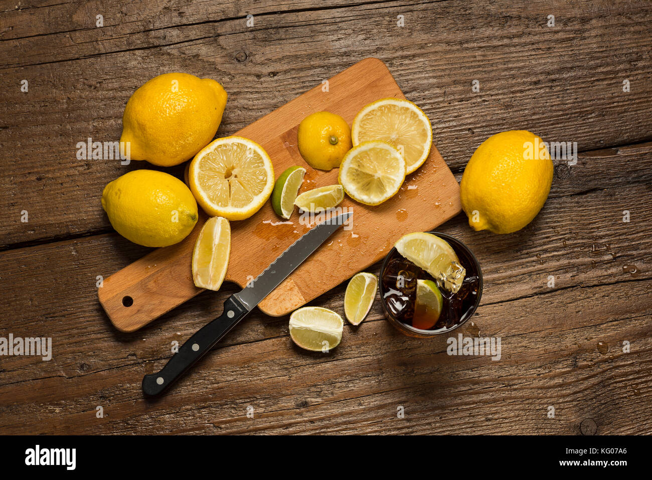 I limoni, coltello e le fette di limone sul tagliere con cocacola vetro su un tavolo di legno. Foto Stock