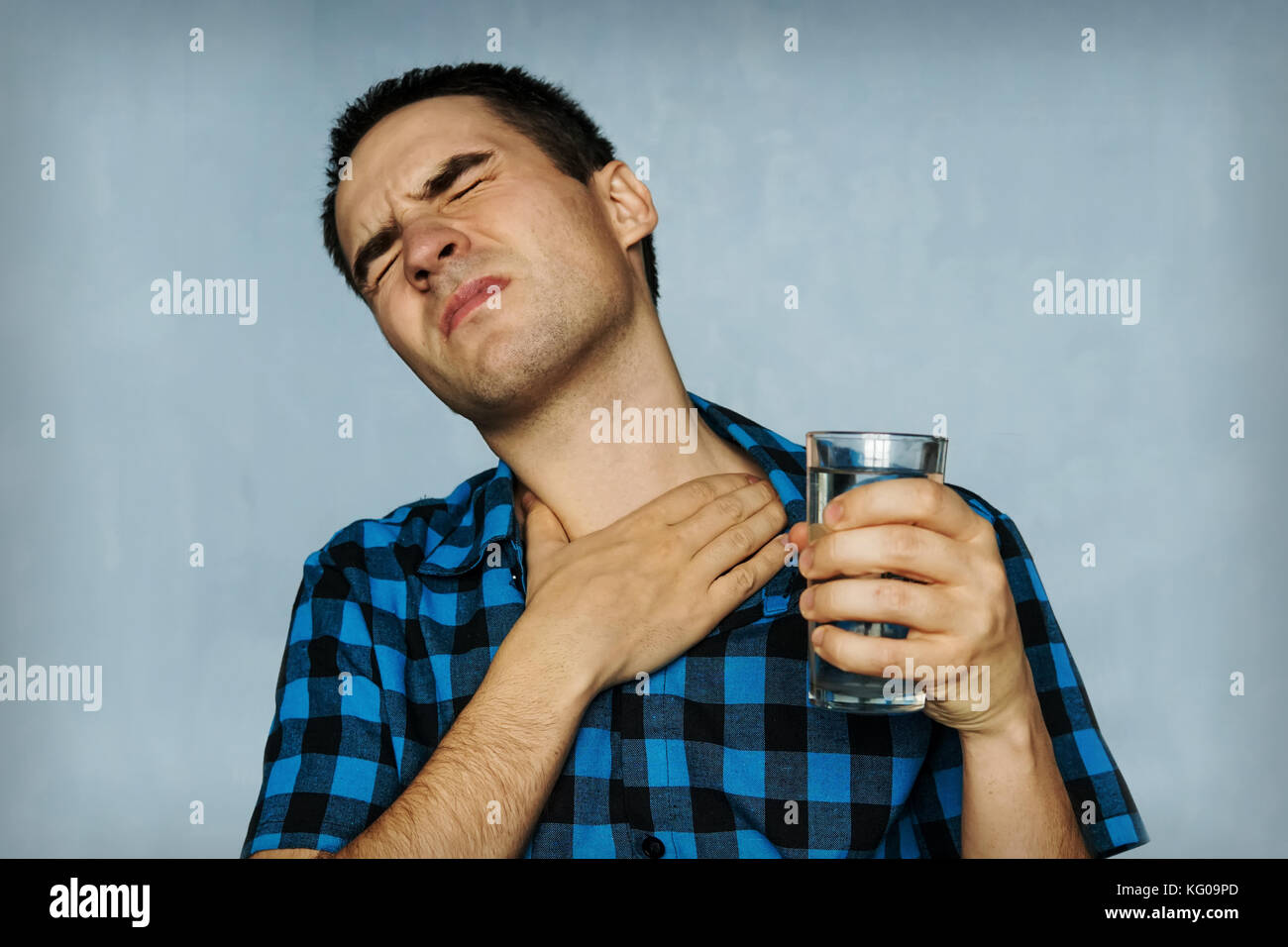 Ritratto uomo tosse, premendo sul petto con espressione dolorosa. Il dolore e il mal di gola durante la malattia influenzale. Il ragazzo con in mano un bicchiere di wat Foto Stock