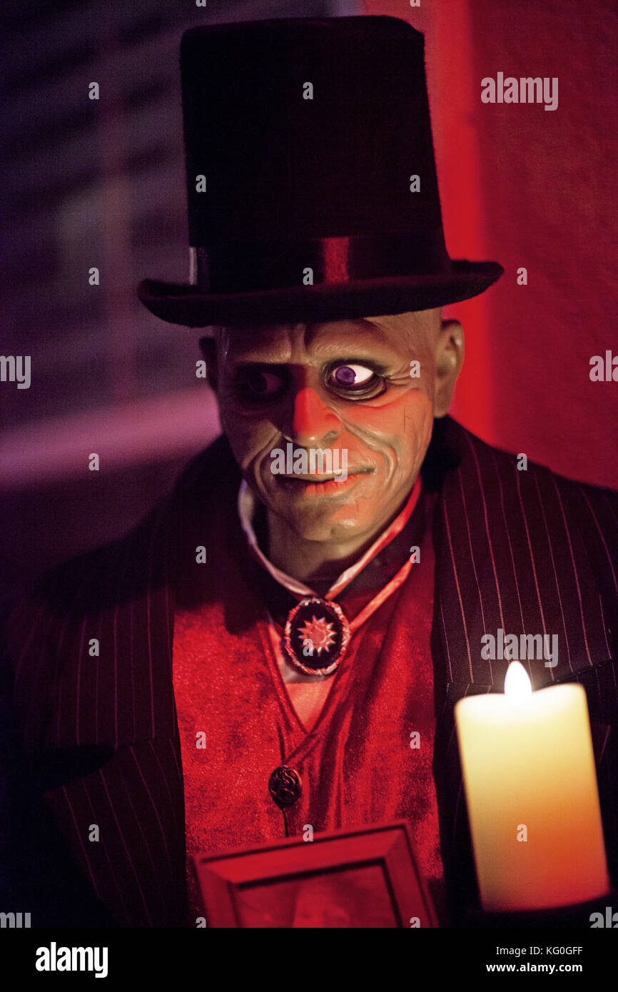 Spaventoso Halloween decorazione di un manichino maggiordomo zombie in un cappello nero top e gilet rosso che tiene una candela Foto Stock