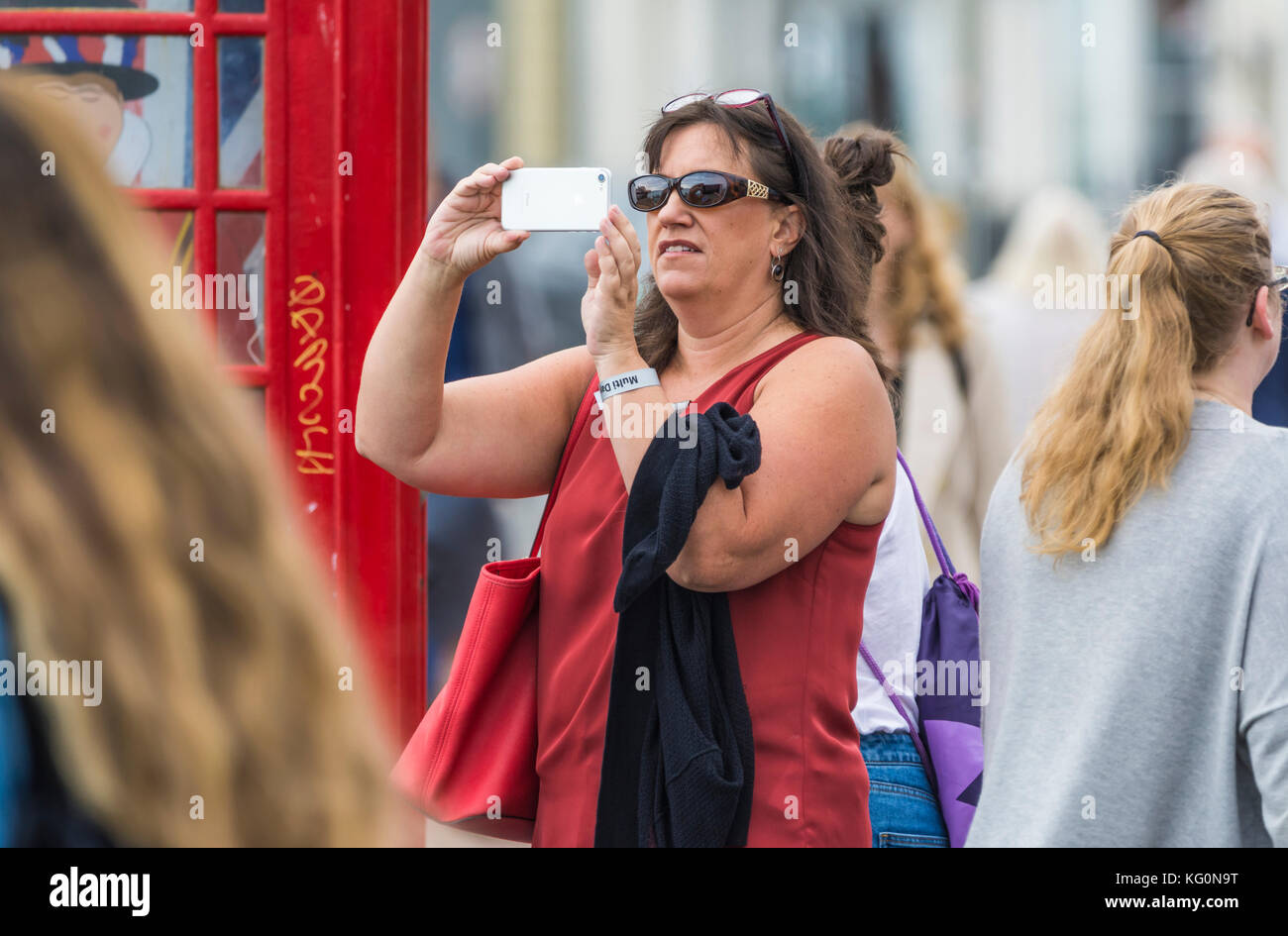 Bianca donna turistica scattare foto utilizzando una fotocamera smartphone in una zona affollata nel Regno Unito. Foto Stock